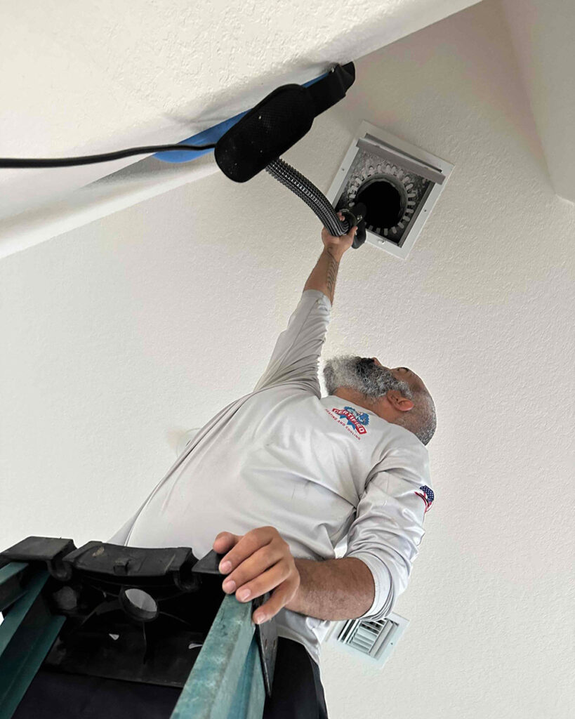 a Certified technician stands on a ladder while cleaning a duct