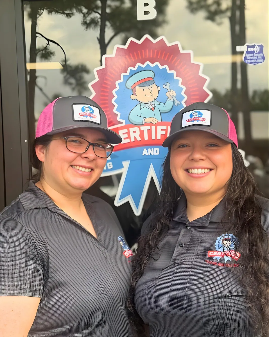 Two women in matching "Certified" hats and shirts smile by a glass door with a "Certified" cartoon logo, showing CSR pride.