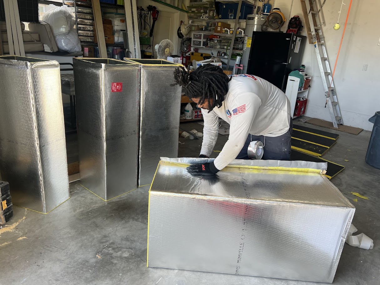 Wearing gloves, a person installs insulation panels in a garage filled with tools and shelves, showing key AC repair skills.