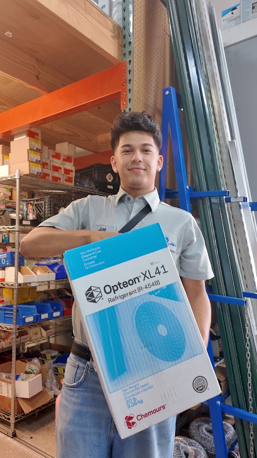 A person holds a Chemours “Opteon XL41 Refrigerant (R-454B)” box in a warehouse with AC repair tools and supplies in Fort Myers.