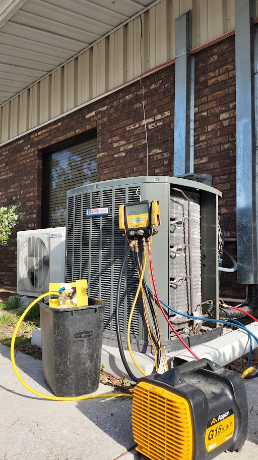 Certified Heating and Cooling technicians service an outdoor AC unit with hoses, gauges, and a yellow recovery machine by a brick building.