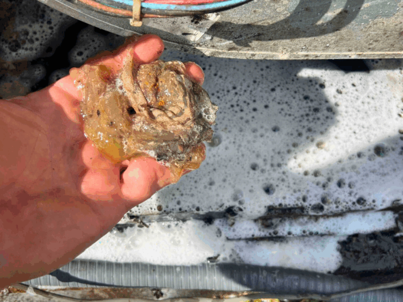 A hand grips a dirty, jelly-like clump from HVAC equipment; soap suds and wires appear in the background.