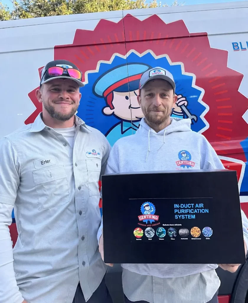 Two men in work uniforms hold an "In-Duct Air Purification System" box by a company van; icons and a cartoon logo decorate it.