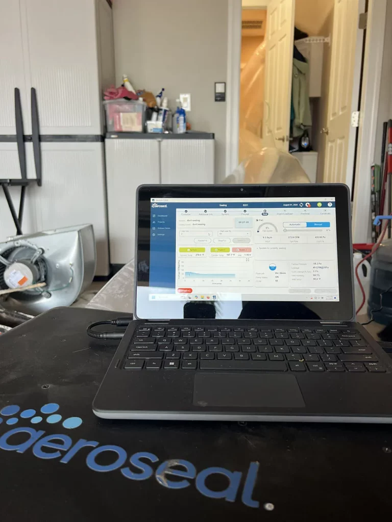 A laptop displays a software dashboard on an Aeroseal-branded surface in a garage with storage cabinets and workshop equipment behind.
