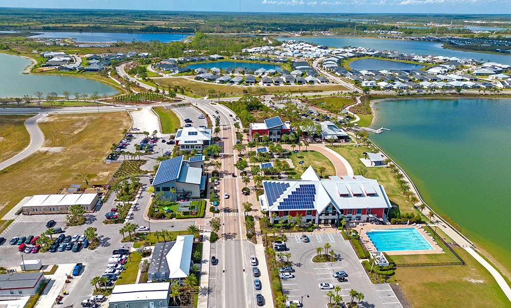 See Babcock Ranch from above with houses, solar buildings, a swimming pool, parking lots, roads, and multiple lakes visible.