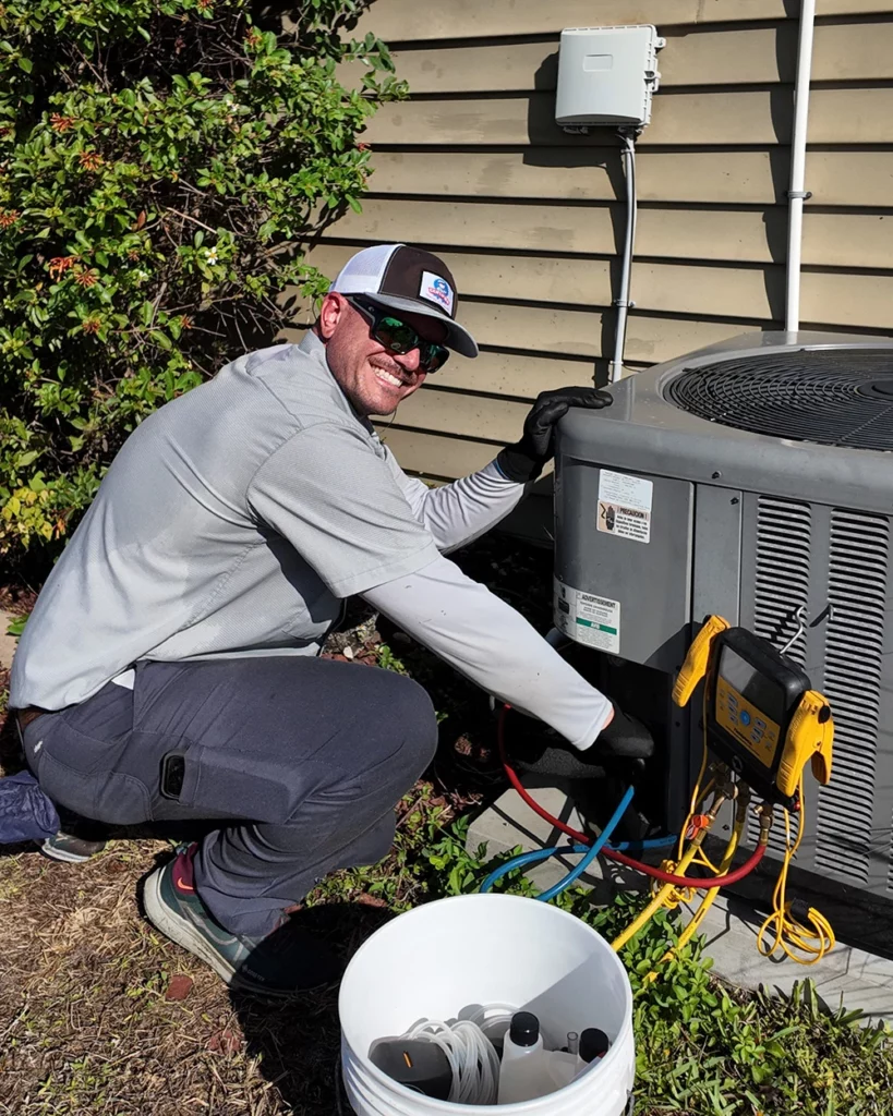 A technician in sunglasses and gloves services a home's AC unit with gauges and tools on a sunny day, ensuring reliable cooling.